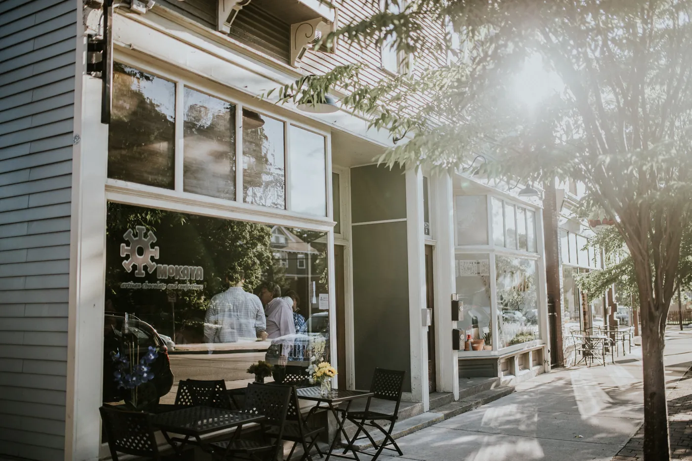 Mokaya's storefront on Wealthy Street at golden hour, with the sun-mark window decal and sidewalk bistro seating.
